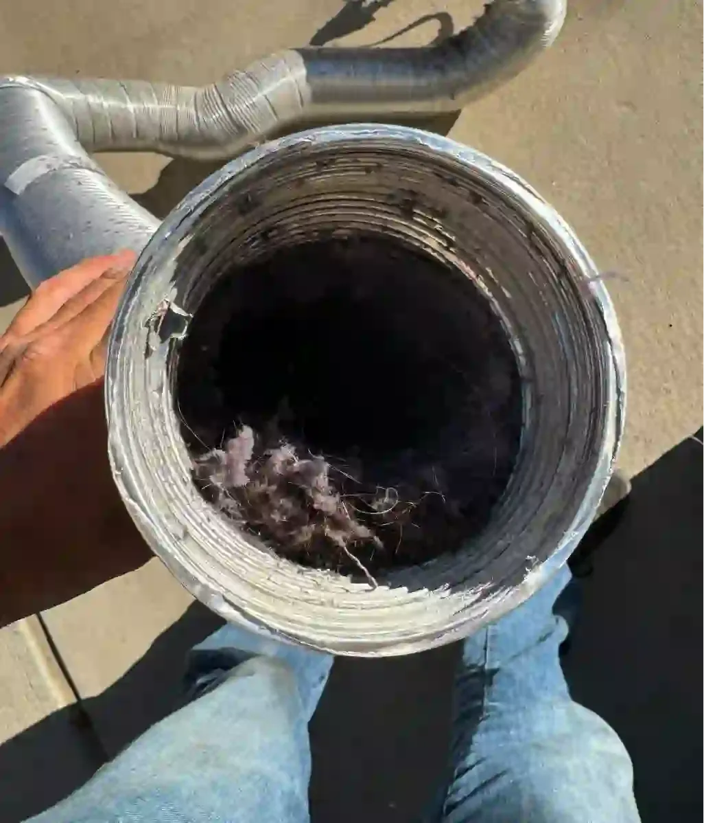 A dryer vent duct packed with grey lint, held up on a job