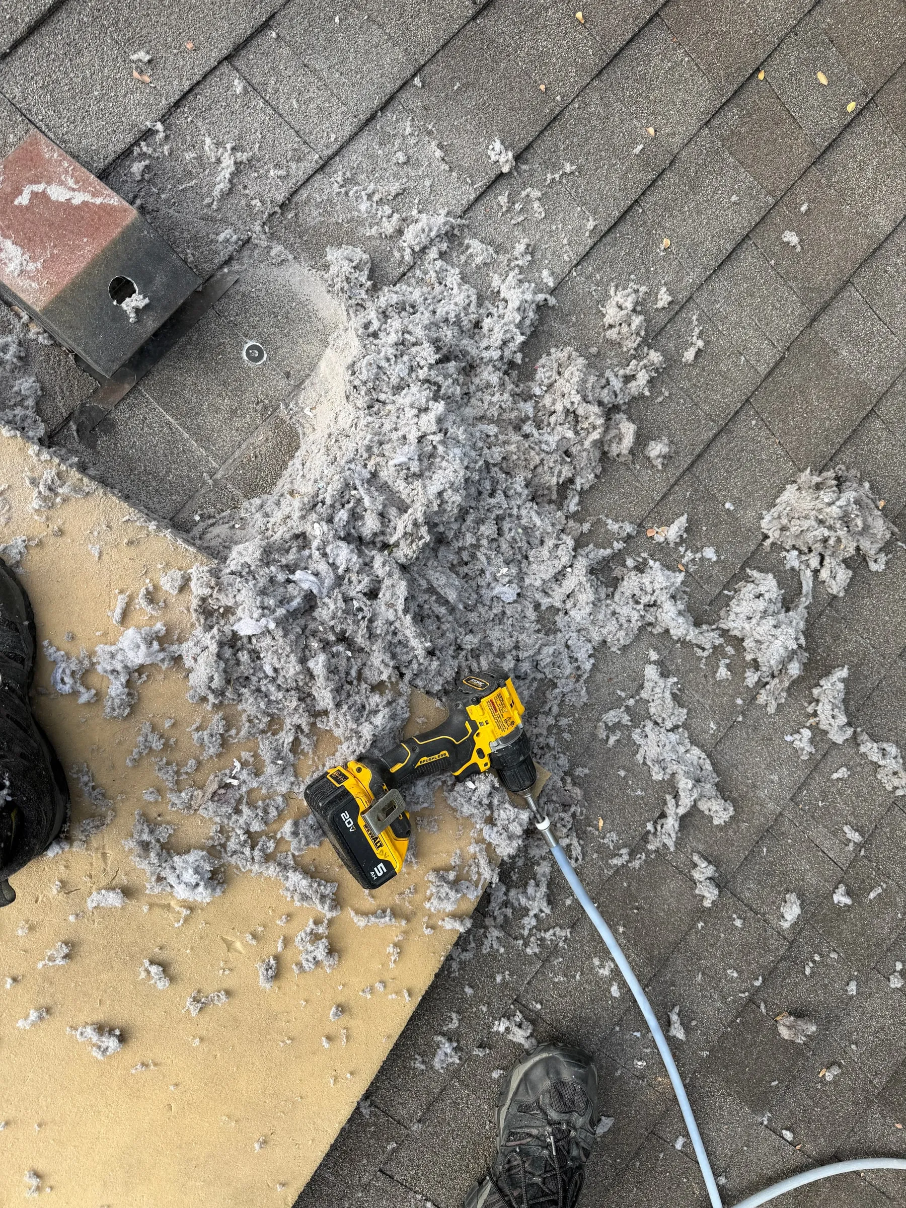 A pile of lint pulled out of a dryer vent onto a shingle roof, with the drill used to clean it