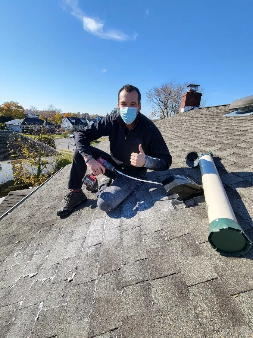 A Dryer Vent Cleaning DFW technician on a shingle roof with a drill and vent brush, giving a thumbs up